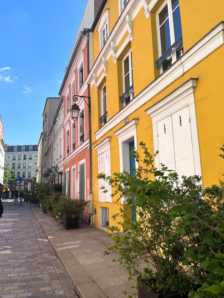 a narrow parisian street featuring colourful houses painting pinks, yellow and blue
