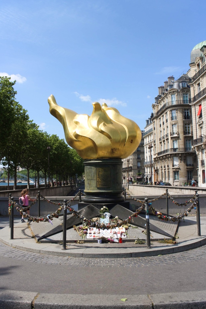 a statue of a flame made from gold on the banks of the river seine